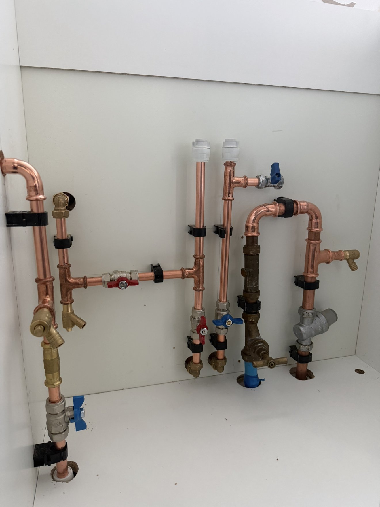 First and second fix plumbing with neatly clipped copper pipework installed under a sink unit